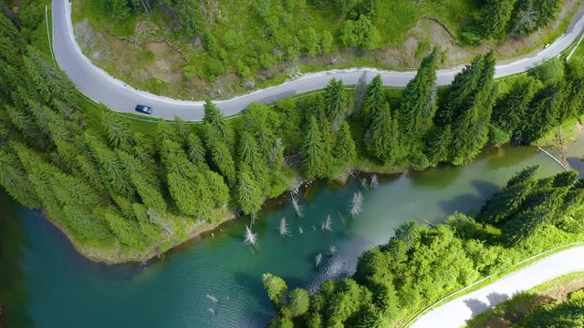 Aerial view of car driving through the fores and the lake on the side. Beautiful mountain road. Driving on the mountain road. Road trip. Mountain forest lake landscape. Car driving through pine forest