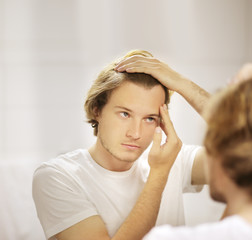 young man looking in the mirror,combing his hair,looking at problems on face