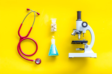 Desk of doctor in laboratory with microscope, stethoscope, test tube for research on yellow...