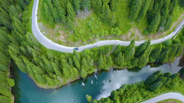 Aerial view of car driving through the fores and the lake on the side. Beautiful mountain road. Driving on the mountain road. Road trip. Mountain forest lake landscape. Car driving through pine forest