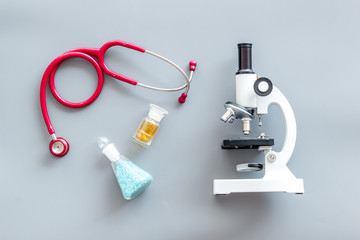Medical tests on work table of doctor with microscope, stethoscope, test tube, pills on gray background top view