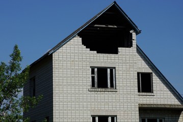 large gray brick unfinished private house with empty windows against a blue sky