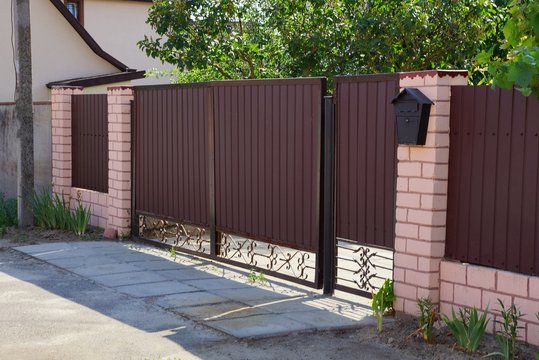 long private brown gates and part of a fence made of metal and bricks in the street