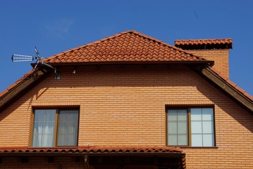 brown brick attic with windows under a tiled roof with a chimney against the blue sky