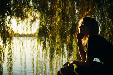 Autumn portrait of smiling young girl near willow on the background of a lake at sunset