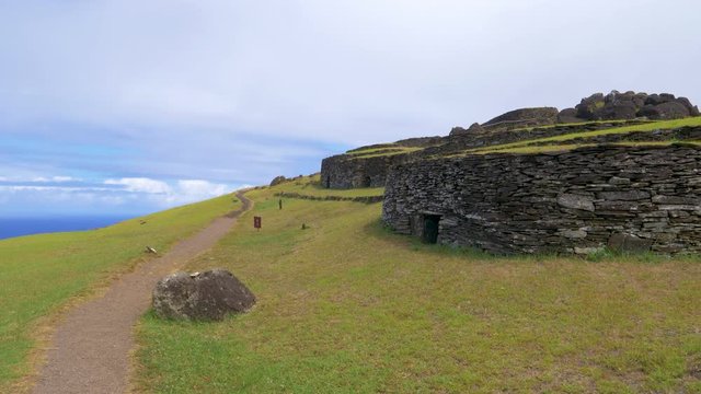 DRONE: Flying above an empty trail leading past the historic village of Orongo. Scenic shot of old stone houses on picturesque Easter Island. Vacant path runs past ancient village on exotic island.