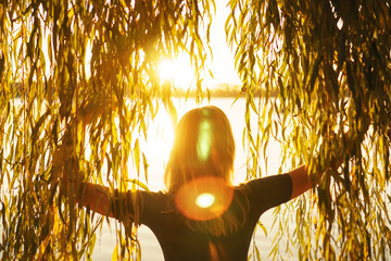 Autumn portrait of young girl with willow branches on the background of a lake at sunset