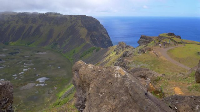 Spectacular shot of volcanic crater of Rano Kau and tourists taking pictures of the landscape and the endless ocean. Travelers visiting crater lake on Easter Island surrounded by steep grassy hills.