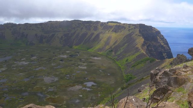 Picturesque view of the cloudy sky spanning above a large volcanic crater on Easter Island. Spectacular shot from above of steep green hills forming a rim around a crater on exotic volcanic island.