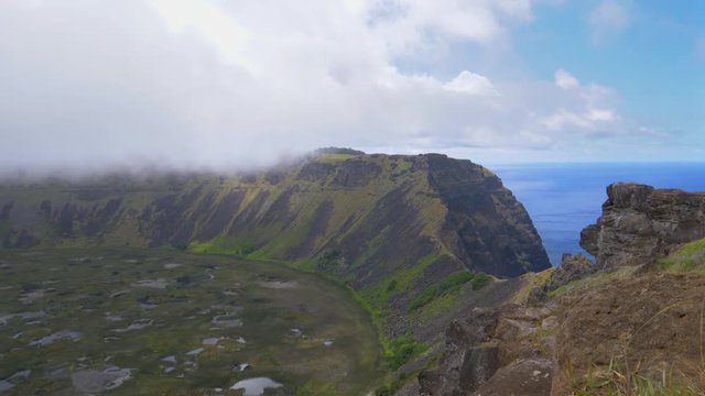 TIMELAPSE: Clouds drift over the massive volcanic crater on the edge of an exotic island in the Pacific. Cinematic shot from above of steep green hills forming a rim around a crater on Easter Island.