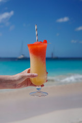 Colorful tiki drink on beach with boats on blue water
