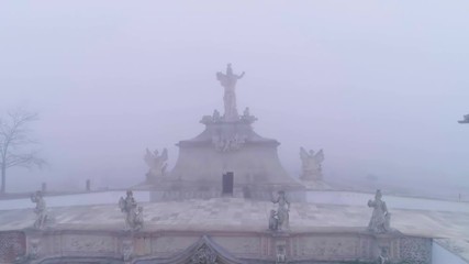 Statue on the top of The 3rd Gate of the Fortress in Alba Iulia. The fortification of largest citadel in Romania. Old stone medieval fortress gate. Foggy day. Aerial view. Silhouette in the fog. 