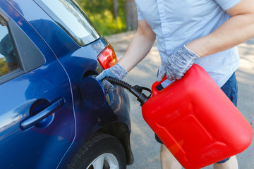 Man pours fuel into the gas tank of his car from a red canister. Driver fills the fuel in an empty tank from a plastic canister. Young man stopped on the side of the road refills the car.