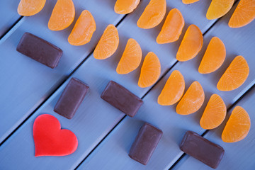 Red heart, chocolates and orange marmalade in the form of mandarin slices lie on a table of painted wooden boards