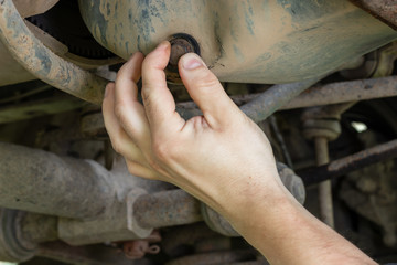Mechanic hand unscrews the cover of the engine crankcase to drain the waste oil.