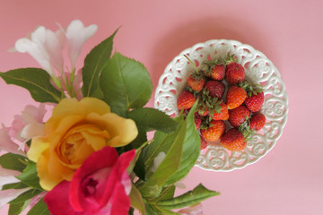 Fresh Strawberries in a White Plate and Flowers isolated on a Pink Background