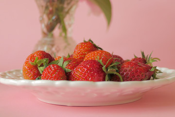 Fresh Strawberries in a White Plate and Flowers isolated on a Pink Background
