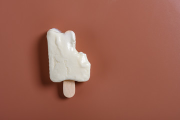 top view mostly eaten milkshake flavor popsicle on a brown background with copy space