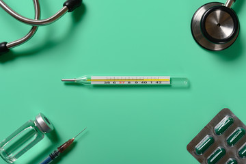 mercury thermometer at  40 degrees centigrade with syringe and vaccine and stethoscope and capsules on the corners