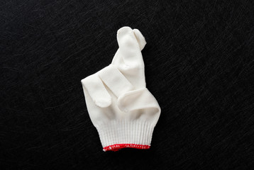 white glove with gesture of fingers crossed on black background