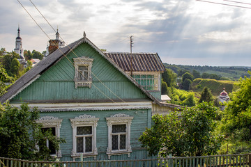 Fototapeta na wymiar Rural wooden house with carved frames in the background of churches in Maloyaroslavets (Malojaroslavec, Maloyaroslavec), Russia - June 2019