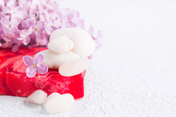 Obraz na płótnie Canvas White stones for massage, red soap and lilac flowers for spa concept. Aromatherapy and relaxation. Selective focus. Copy space