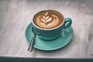 Cappuccino coffee cup at trendy cafe with latte art in foam on top of espresso drink in trendy blue mug on tabletop.