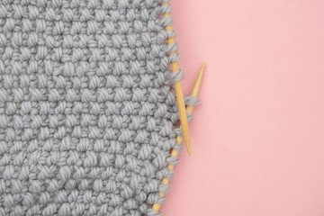Piece of grey knitted fabric on bamboo wood needles, process of knitting close up on pink background with copy space for text. Top view Flat lay Template for your design