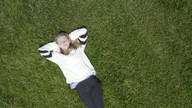 Young girl laying in grass overhead aerial 4k