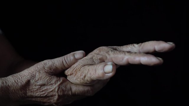 Close up old woman massages painful and itching hands with the black background.