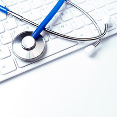 Blue stethoscope on computer keyboard on white table background. Online medical information treatment technology concept, close up, macro, copy space