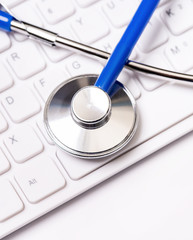 Blue stethoscope on computer keyboard on white table background. Online medical information treatment technology concept, close up, macro, copy space