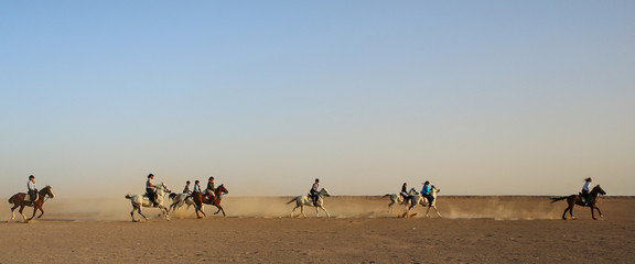 Fototapeta na wymiar A group of people racing across the desert on Arabian horses. 