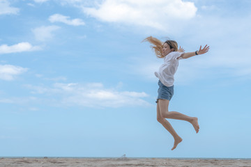 female making jump on sandy beach with blue sky