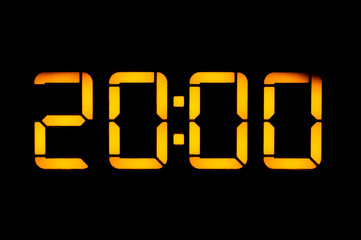 Electronic digital clock with orange numbers on a black background shows the time Twenty zero zero in the evening. Isolate, close-up.