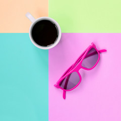 Small white coffee cup and pink sunglasses on background of fashion pastel pink, blue, coral and...