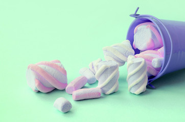 Overturned miniature lilac bucket filled with marshmallow lies on a turquoise pastel background