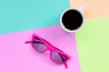 Small white coffee cup and pink sunglasses on background of fashion pastel pink, blue, coral and...
