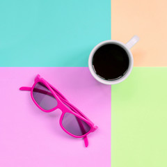 Small white coffee cup and pink sunglasses on background of fashion pastel pink, blue, coral and...