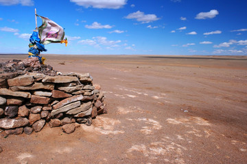 Ovoo, oboo or obo (ceremonial rock pile or cairn) with sacred hadags or khadags (blue silk scarves) and a large prayer flag on top in the Gobi desert, Mongolia.