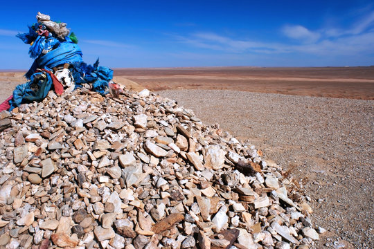 Ovoo, oboo or obo (ceremonial rock pile or cairn) with sacred hadags or khadags (blue silk scarves) with a goat skull on a pile of rocks in the Gobi desert, Mongolia.