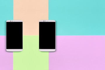 Two modern smartphones with black screens on background of fashion pastel pink, blue, coral and...