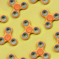 Many orange fidget spinners lies on texture background of fashion pastel orange color paper