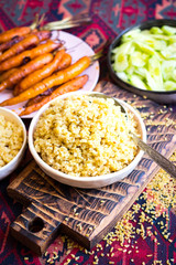 Cooked bulgur - traditional Arabic food from Middle Eastern cuisine. Baked carrots vegetables. Vegan, vegetarian healthy diet. On red eastern pattern background.