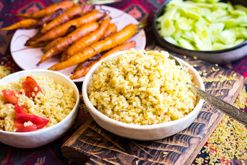 Cooked bulgur - traditional Arabic food from Middle Eastern cuisine. Baked carrots vegetables. Vegan, vegetarian healthy diet. On red eastern pattern background.