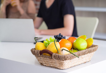 Close-up of basket with colorful fruits on table with young couple blurred background