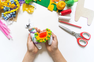 The hands of the child diy do handicraft toy lama. Felt soft craftsmanship.