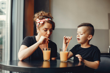 Family in a cafe. Mother in a black t-shirt. Cute little boy drinking a juice