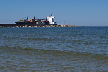 Blue hulled cargo ship loaded with shipping containers of various colors enters the coastal Bay...