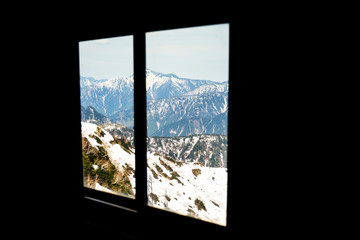 The ice-covered mountains in the late winter are seen from the window in a dark room.